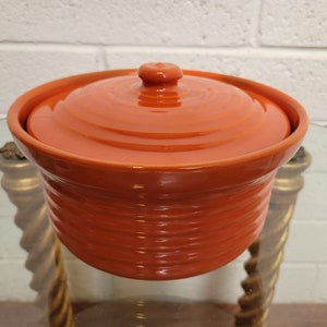 May include: Orange ceramic container with a lid. The container has a ribbed design and the lid has a smooth, rounded top.