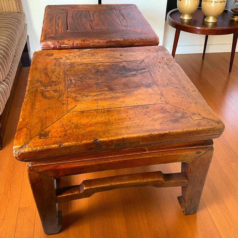 May include: Two antique wooden side tables. The tables have a square top with a rectangular frame and a dark brown finish. The legs are sturdy and have a unique design. The tables are placed on a hardwood floor.