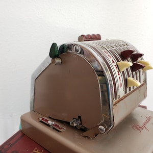 May include: A vintage brown and silver cash register with a Paymaster label. The register has a series of numbered keys and a green lever.