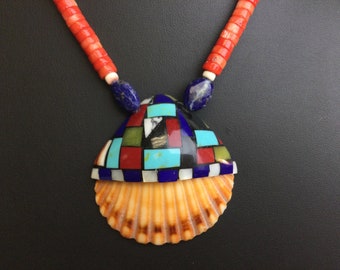 May include: A Native American-style necklace with a shell pendant. The pendant is decorated with a mosaic of turquoise, red, blue, green, and white stones. The necklace is made of red coral beads.