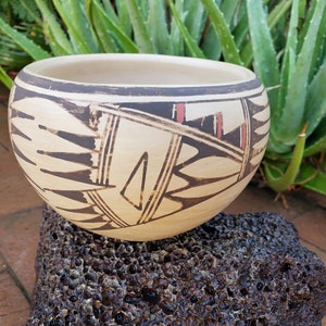 May include: A white ceramic bowl with black and red geometric designs. The bowl is sitting on a dark brown rock.