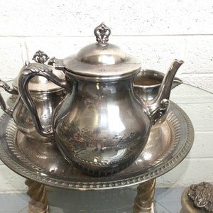 May include: A silver tea set with a teapot, creamer, and sugar bowl on a silver tray. The set has an ornate design and is in excellent condition.