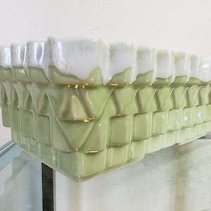 May include: Rectangular ceramic planter in a light green hue with a textured, woven-like pattern. The top edge features a white glaze, creating a two-tone effect. The planter is designed for indoor or outdoor use.