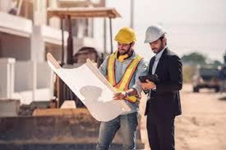 May include: Two men at a construction site examining blueprints. One wears a yellow hard hat and safety vest, holding the plans. The other wears a white hard hat and a suit, holding a tablet. A bulldozer is visible in the background.