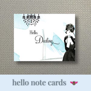 May include: A white note card with the text "Hello, Darling" in elegant script, featuring a black and white illustration of a woman in a black dress and a chandelier. Light blue watercolor accents add a touch of color.