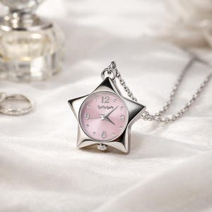 May include: A silver star-shaped pendant watch with a pink face and a silver chain. The watch has a classic analog display with the numbers 12, 3, 6, and 9 clearly visible. The watch is a stylish accessory.