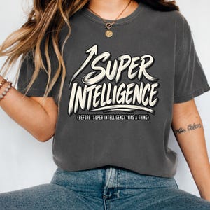 Puede incluir: Una camiseta de manga corta gris carbón con el texto blanco "SUPER INTELLIGENCE" en una fuente estilo pincelada, una flecha que apunta hacia arriba y el texto más pequeño "(BEFORE 'SUPER INTELLIGENCE' WAS A THING)" impreso debajo.