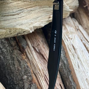 Puede incluir: Primer plano de gafas de sol negras con el texto "cff S 3020 KOREA" impreso en la patilla. Las gafas de sol est&aacute;n sobre un fondo de madera marr&oacute;n texturizada.