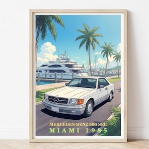 Op de afbeelding: Een ingelijste print met een witte Mercedes-Benz 500 SEC coupé uit 1985, geparkeerd op een weg met palmbomen en jachten op de achtergrond. De print heeft de tekst "Mercedes-Benz 500 SEC Miami 1985" onderaan.