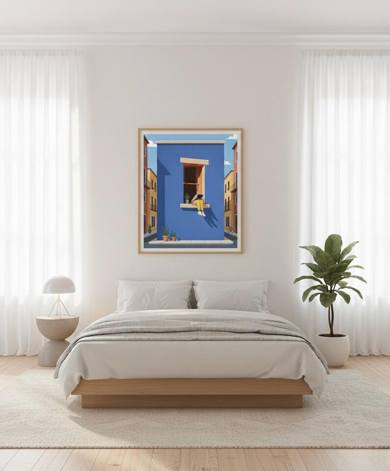 May include: A framed art print depicts a person in a yellow outfit sitting in a window, overlooking a street scene with buildings. The artwork has a blue wall and a wooden frame. The room has a bed, a side table with a lamp, and a potted plant.