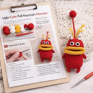 May include: A clipboard with instructions for an "Ugly-Cute Pull Keychain Monster" crochet project, featuring a finished red monster with yellow accents. The finished size is approximately 3 inches. A crochet hook and yarn are also visible.