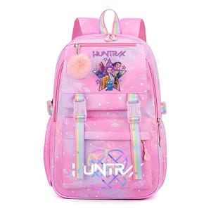 May include: Pink backpack with a colorful design, featuring the text "HUNTRA" and a star-shaped graphic with characters. The backpack has adjustable straps, a top handle, and a fluffy pink pom-pom. It is designed for school or travel.