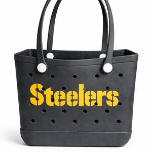 May include: Black tote bag with the word "Steelers" in yellow stencil lettering. The bag has two black handles and white circular accents. The bag has several small circular holes.