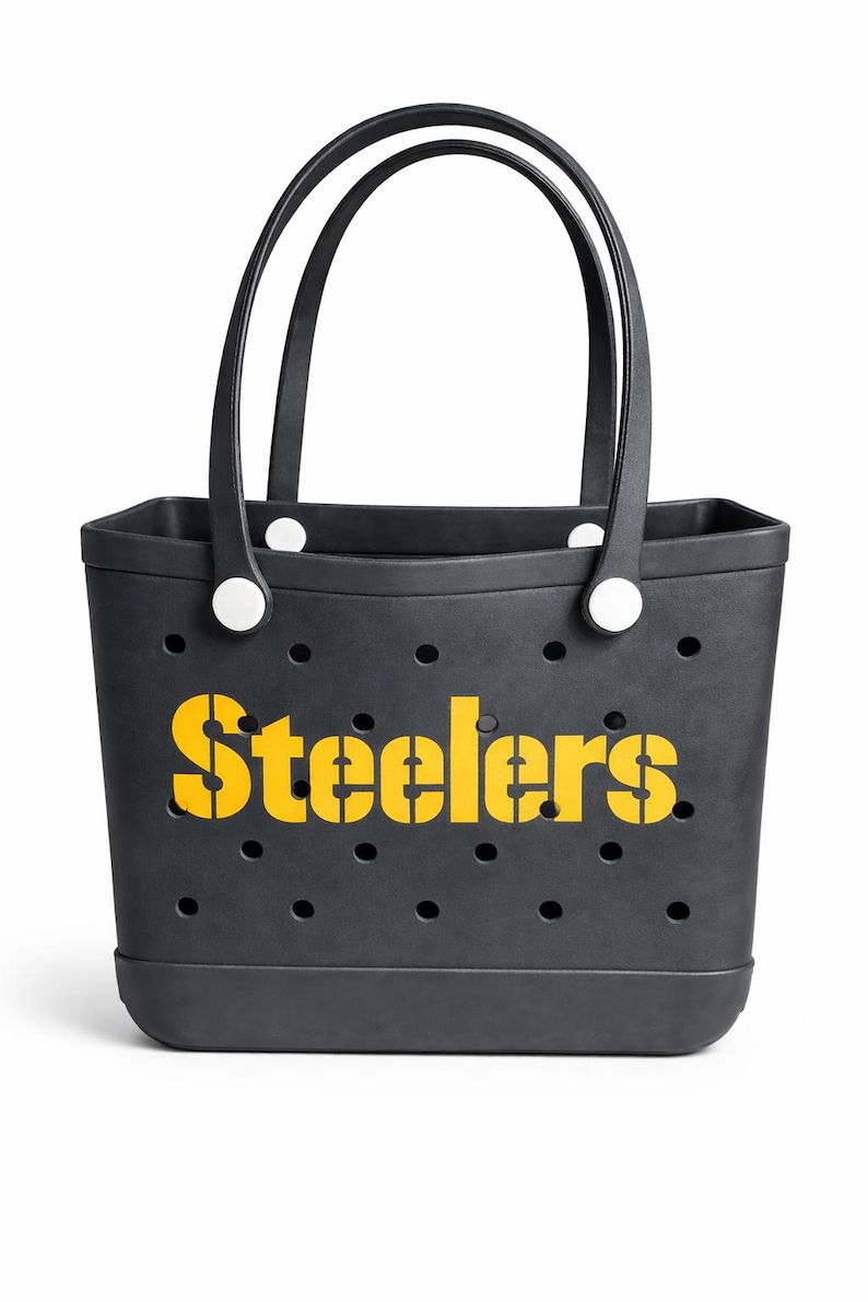 May include: Black tote bag with the word "Steelers" in yellow stencil lettering. The bag has two black handles and white circular accents. The bag has several small circular holes.