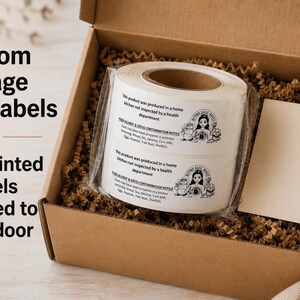 May include: A roll of white adhesive food labels featuring black text and a small illustration of a baker, packaged inside a brown cardboard box filled with shredded paper filler, alongside a blank rectangular card and promotional text.