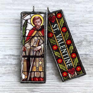 May include: Two stained glass window ornaments, one depicting Saint Valentine with a sword and the other with the text "ST. VALENTINE" and red hearts.