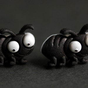 May include: A pair of black ant earrings with white googly eyes. The ants are made of polymer clay and have a textured surface.