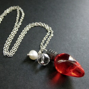 May include: A silver chain necklace with a red glass lightbulb pendant, a white pearl bead, and a clear crystal bead.