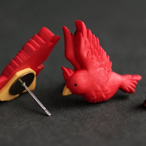 Puede incluir: Un par de pendientes de p&aacute;jaro cardenal rojo con un poste y una parte posterior de bronce. Los pendientes est&aacute;n hechos de arcilla polim&eacute;rica y miden aproximadamente 2,5 cm.