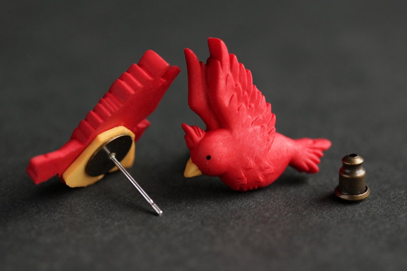 Puede incluir: Un par de pendientes de p&aacute;jaro cardenal rojo con un poste y una parte posterior de bronce. Los pendientes est&aacute;n hechos de arcilla polim&eacute;rica y miden aproximadamente 2,5 cm.