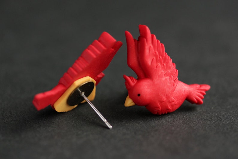 Puede incluir: Un par de pendientes de p&aacute;jaro cardenal rojo. Los pendientes est&aacute;n hechos de arcilla polim&eacute;rica y tienen un dise&ntilde;o realista. Los pendientes est&aacute;n unidos a postes de plata.