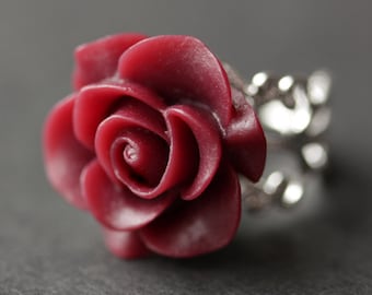 May include: A burgundy rose ring with a silver chain design. The rose is made of polymer clay and is a statement piece.