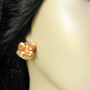 May include: A pair of copper butterfly earrings. The earrings are a light orange color and have a textured surface.