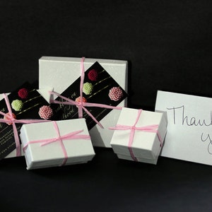May include: Four white gift boxes tied with pink ribbon and decorated with pink and green flowers. A white card with the text "Thank you!" is in the foreground.