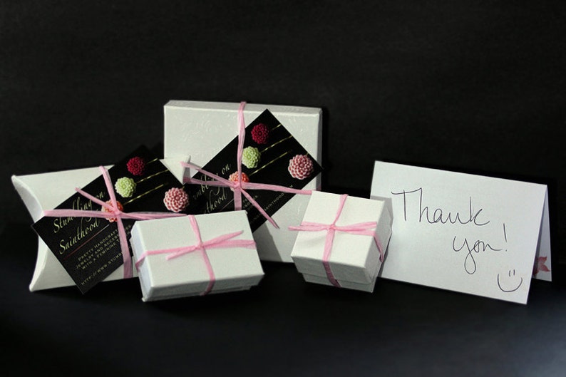 May include: Four white gift boxes tied with pink ribbon and decorated with pink and green flowers. A white card with the text "Thank you!" is in the foreground.