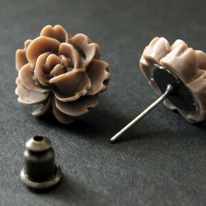 May include: A pair of brown flower-shaped stud earrings with silver posts. The earrings are made of polymer clay and have a realistic flower design.