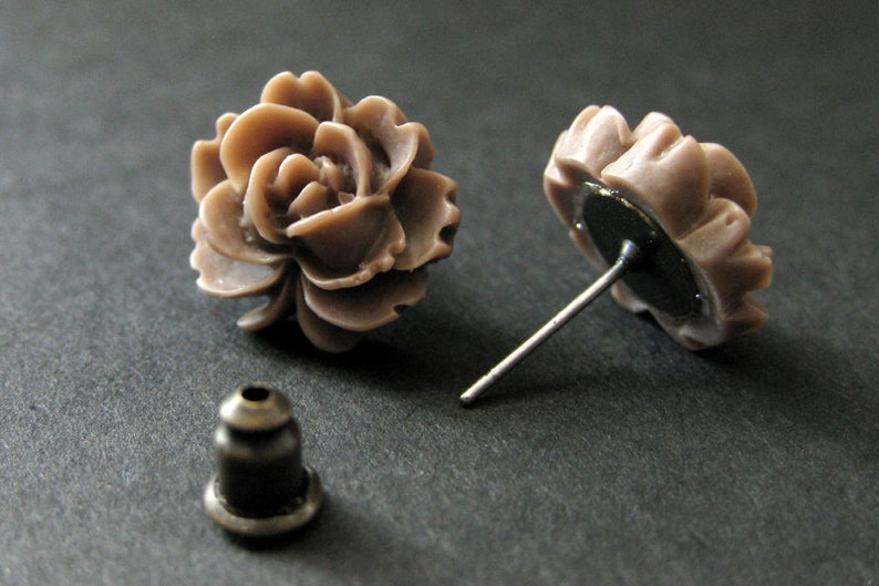 May include: A pair of brown flower-shaped stud earrings with silver posts. The earrings are made of polymer clay and have a realistic flower design.
