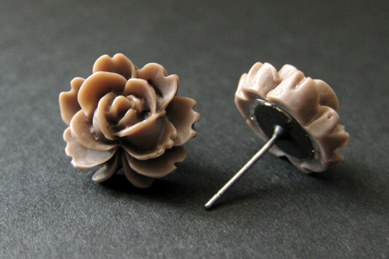 May include: A pair of brown rose-shaped stud earrings. The earrings are made of a smooth, matte material and have a simple, elegant design.