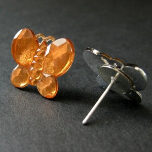 May include: A pair of orange butterfly stud earrings with silver posts. The butterfly design is made of faceted rhinestones.