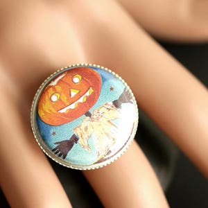 May include: A silver ring with a blue and white cameo featuring a jack-o'-lantern with a smiling face. The cameo is surrounded by a silver band.