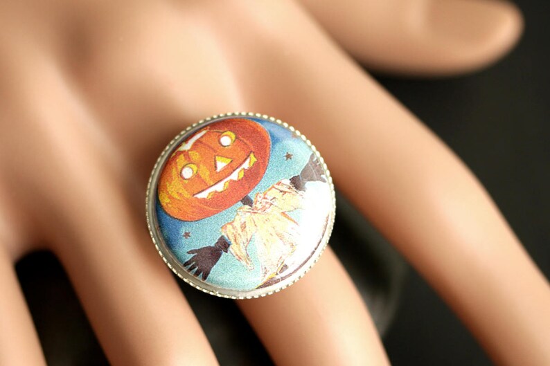 May include: A silver ring with a blue and white cameo featuring a jack-o'-lantern with a smiling face. The cameo is surrounded by a silver band.