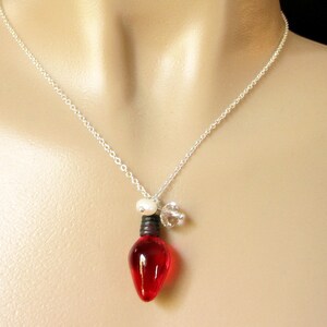 May include: A silver chain necklace with a red glass lightbulb pendant, a white pearl bead, and a clear crystal charm.