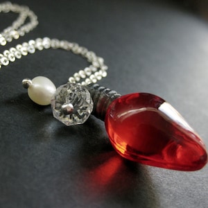 May include: A silver chain necklace with a red glass lightbulb pendant, a white pearl bead, and a clear crystal bead.