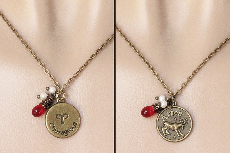 Może przedstawiać: Złoty naszyjnik z zawieszką przedstawiającą astrologiczny symbol Barana, barana. Zawieszka zawiera r&oacute;wnież napis "Aries" i "Odważny". Naszyjnik ma czerwone i białe koraliki.