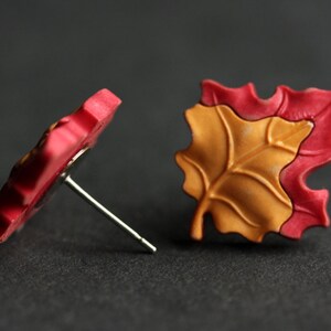 Pu&ograve; includere: Un paio di orecchini a forma di foglia rossa e arancione con perni d'argento. Gli orecchini sono realizzati in pasta polimerica e hanno una superficie testurizzata.