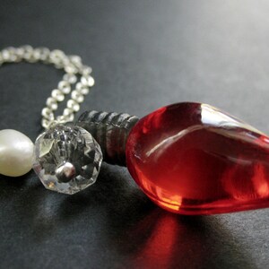 May include: A silver chain necklace with a red glass lightbulb pendant, a white pearl bead, and a clear crystal bead.