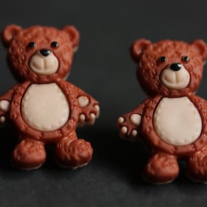 Pode incluir: Dois botões de urso de peluche castanhos com barriga bege e olhos pretos.