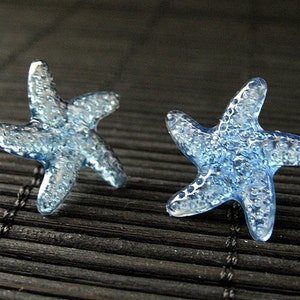 May include: A pair of blue glass starfish earrings. The starfish are textured and have a slightly iridescent finish.