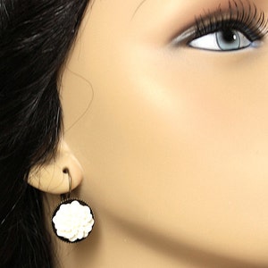 May include: A pair of dangle earrings with a white flower design on a black background. The earrings are made of metal and have a hook closure.