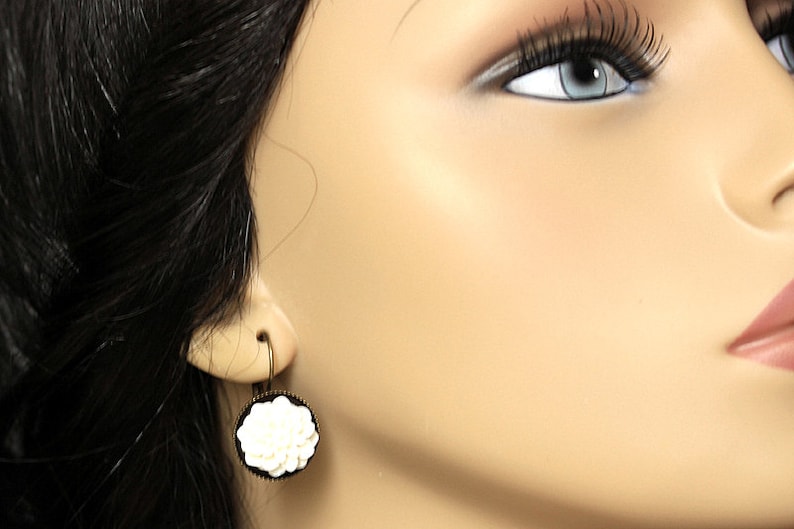 May include: A pair of dangle earrings with a white flower design on a black background. The earrings are made of metal and have a hook closure.