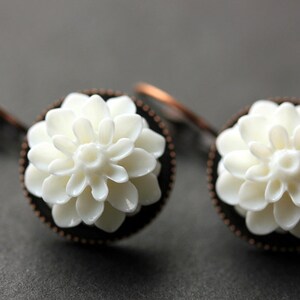 May include: A pair of white flower earrings with copper-toned settings. The flowers are made of white ceramic and have a delicate, intricate design.