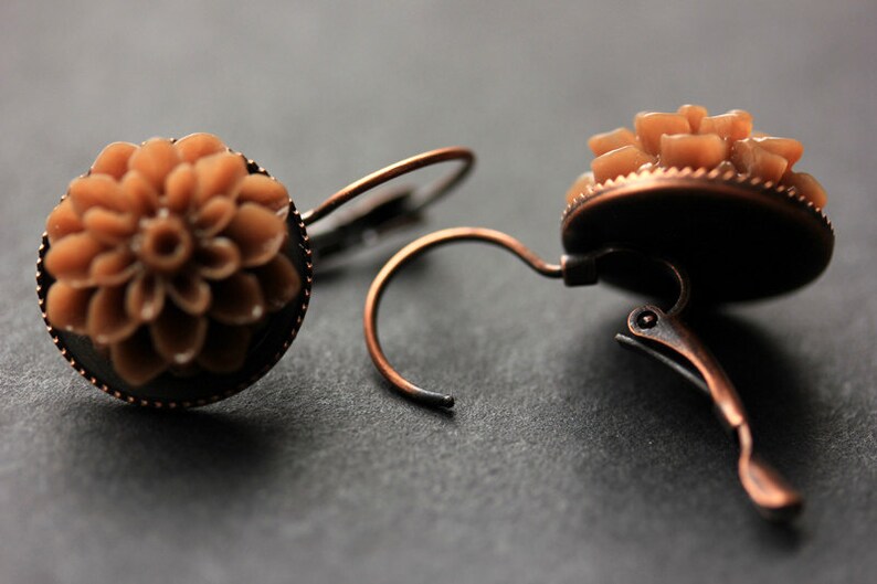 Puede incluir: Un par de pendientes de color marr&oacute;n y cobre con un dise&ntilde;o floral. Los pendientes est&aacute;n hechos de metal y tienen un cierre de clip.