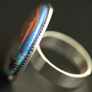 May include: A silver ring with a blue and orange enamel design. The ring has a wide band and a raised design.