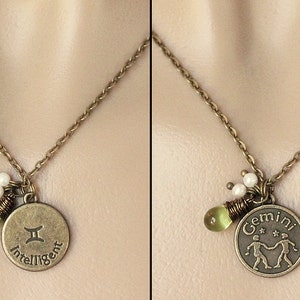 May include: A gold necklace with a round pendant featuring the Gemini zodiac symbol and the word "Intelligent". The pendant is accented with green and white beads.