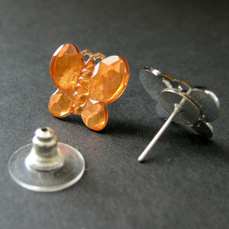 May include: A pair of orange butterfly stud earrings with silver posts and backs. The butterfly design is made of faceted plastic.