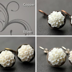 May include: Two pairs of earrings with white flower-shaped charms. The earrings are on a gray background. The top pair has copper hooks and the bottom pair has bronze hooks.